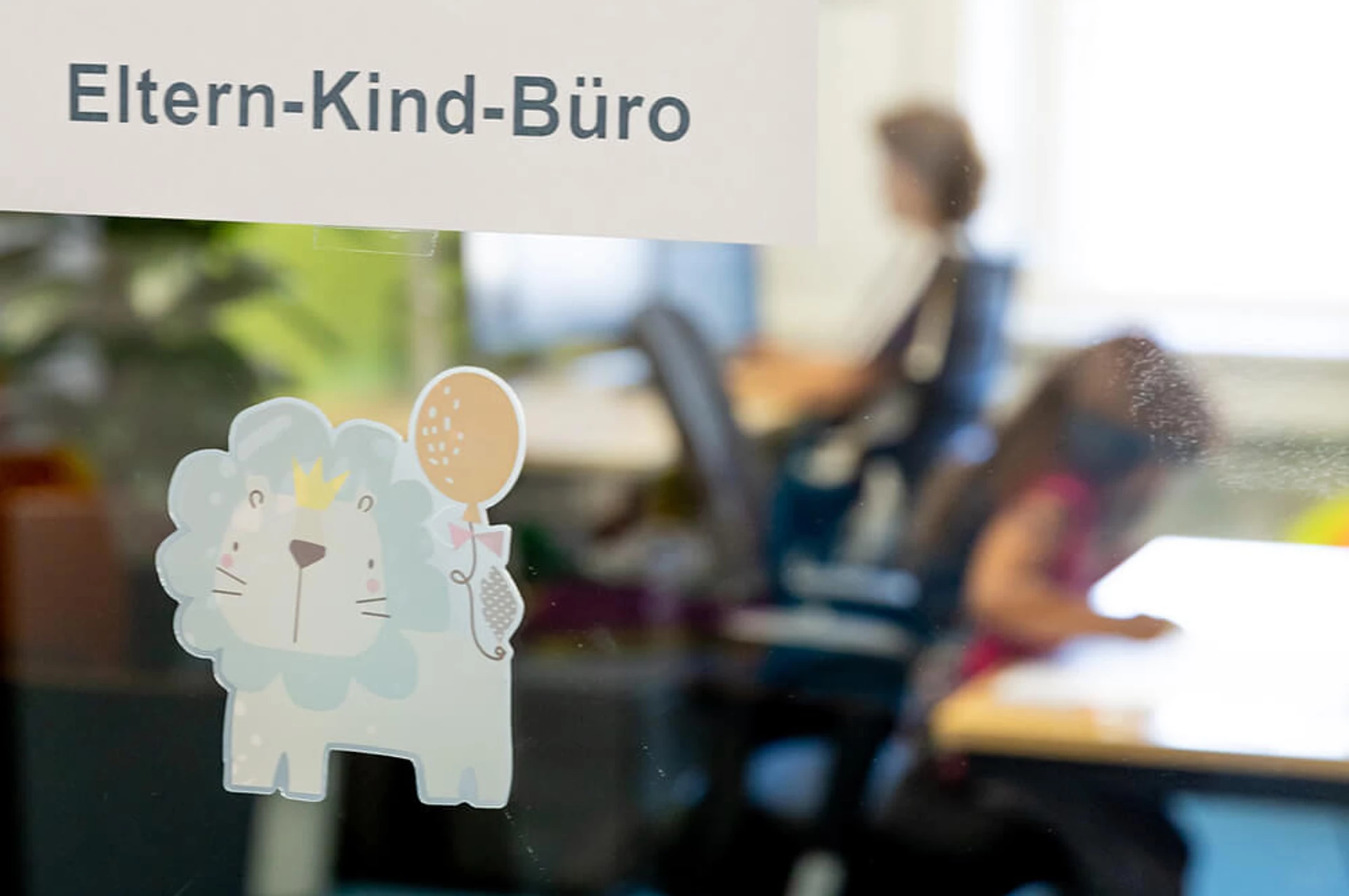 Eltern-Kind-Büro Schild mit einer Mitarbeiterin und ihrer Tochter am Schreibtisch